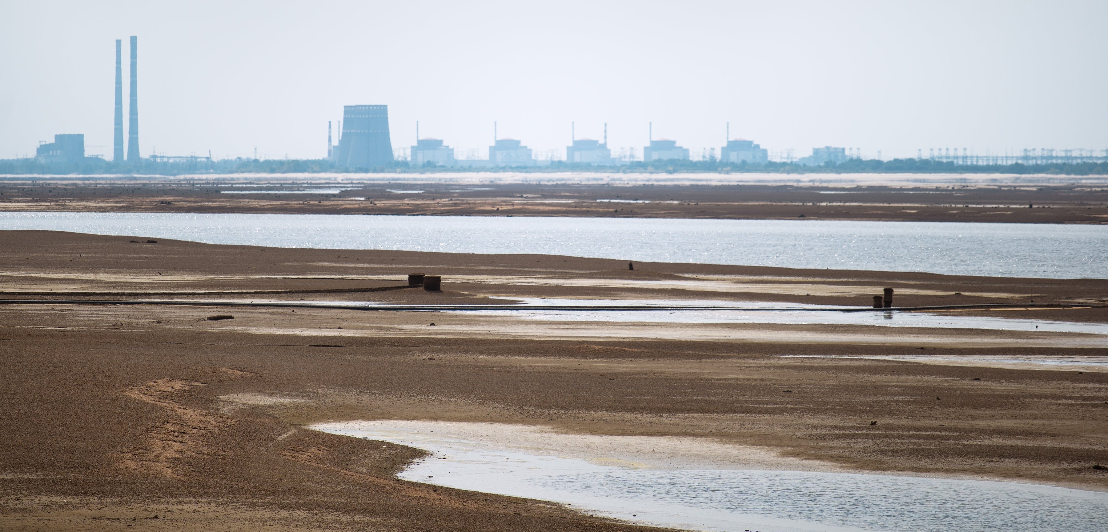 Disig bilde med vanndammer og sandbanker i forgrunnen, lengst bak i bildet ser man kjernekraftverket Zaporizjza.